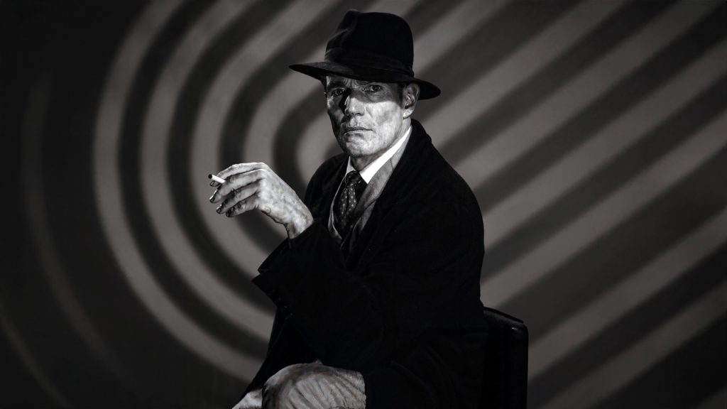Richard Pate as the Devil in Black Chariot, wearing a hat and dark suit