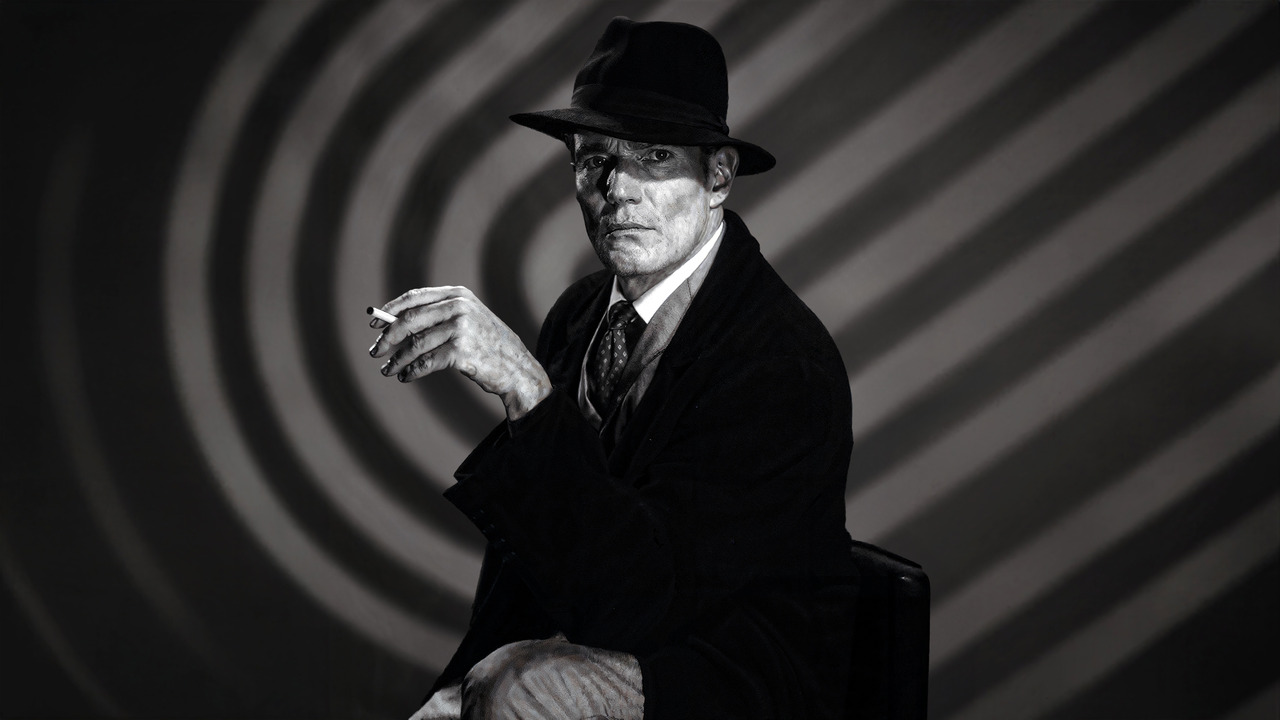 Richard Pate as the Devil, wearing a dark hat and suit in Black Chariot