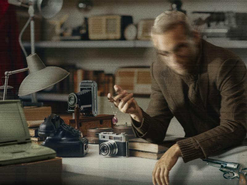 Uncle Monty’s Antique Shop promotional artwork showing its proprietor behind a counter of old cameras, books and curiosities.