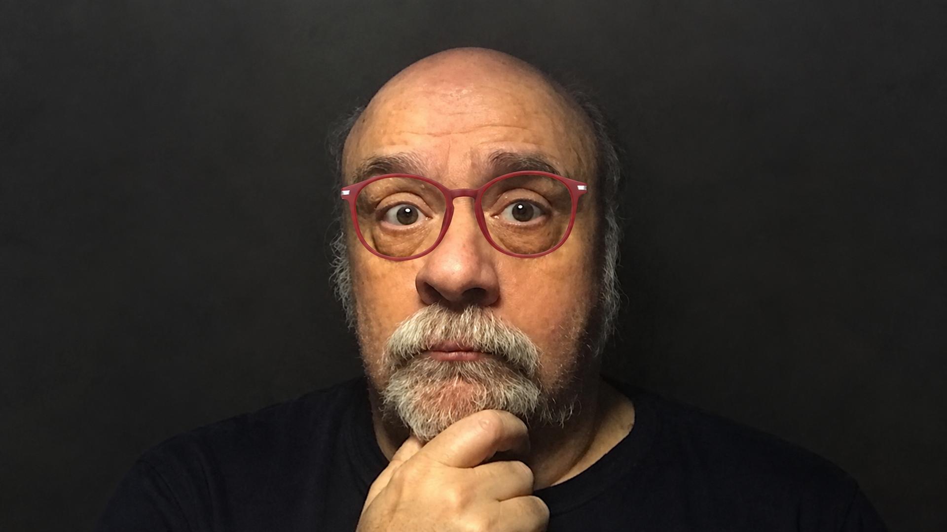 Composer Joseph Renzetti wearing red glasses, with his hand resting beneath his chin.