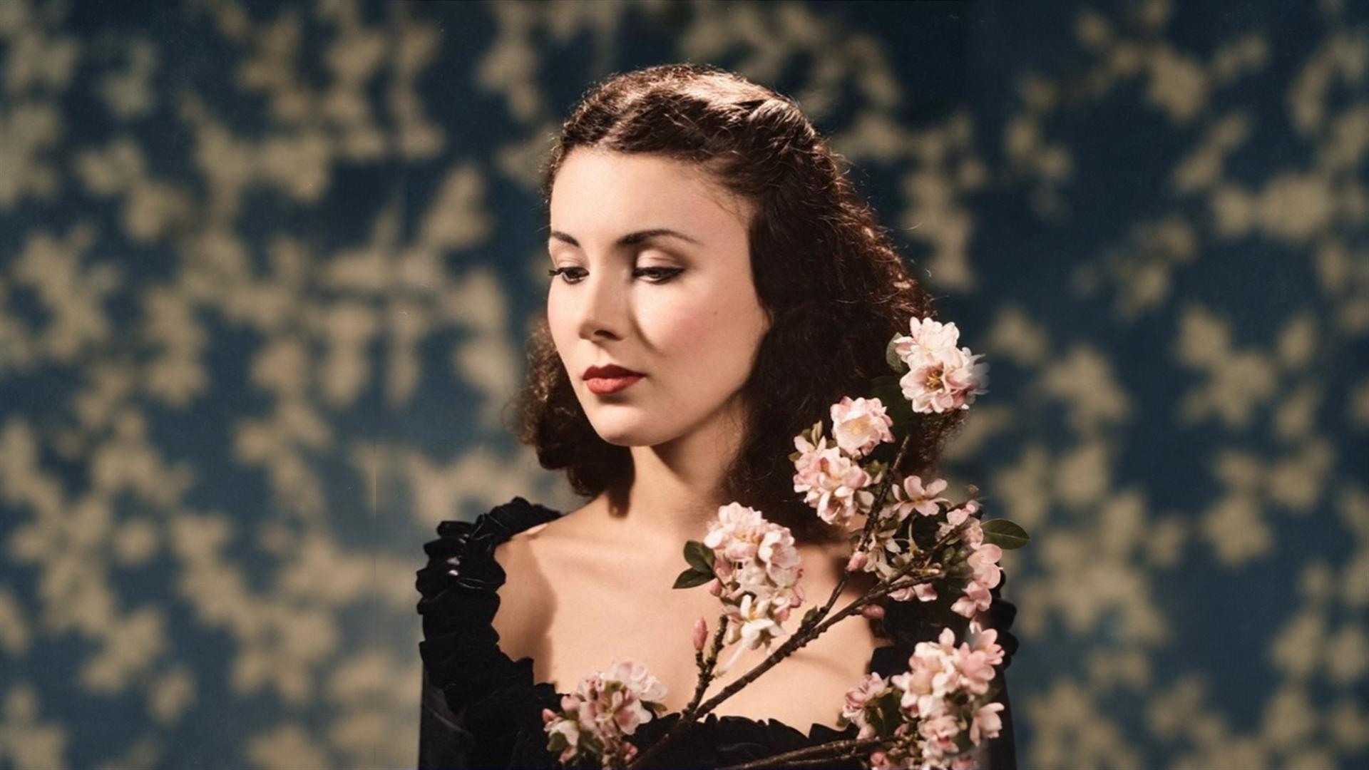 Megan Tremethick looking down beside pink blossoms in a portrait inspired by classic cinema.